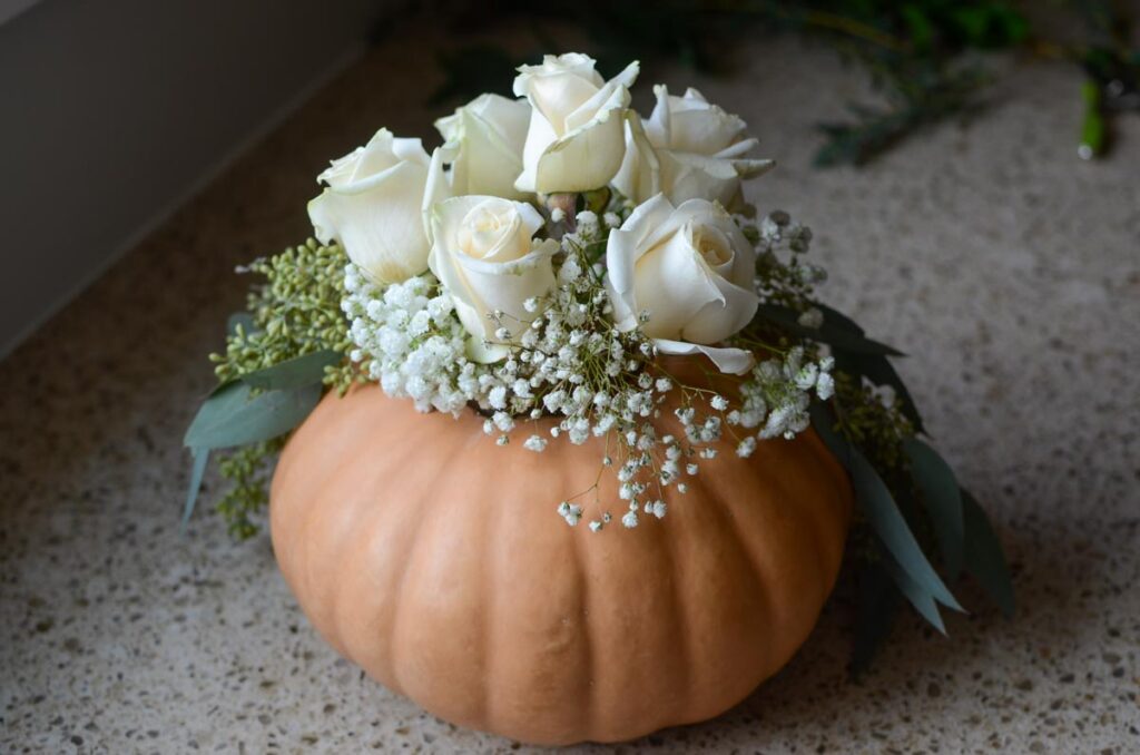 adding flowers to the pumpkin floral arrangement