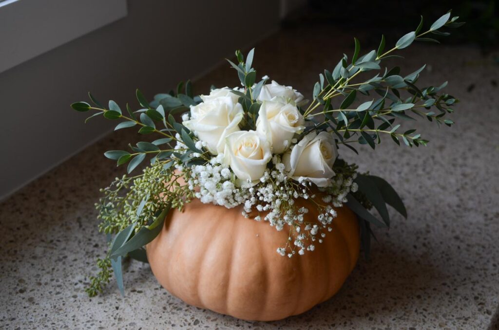 adding flowers to the pumpkin flower arrangement