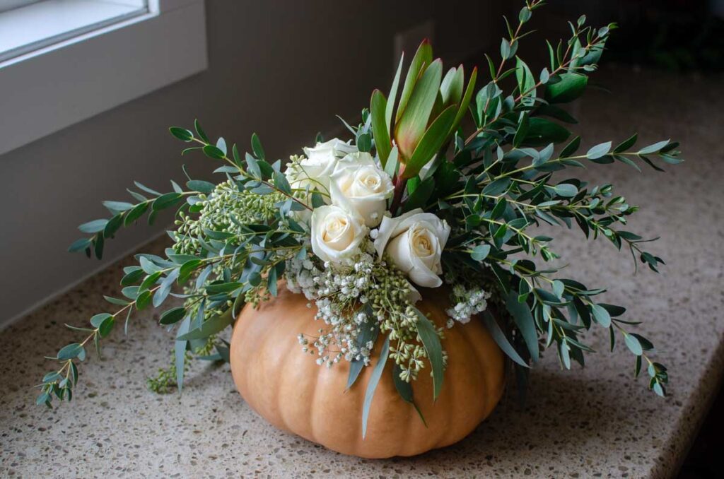 adding flowers and greenery to the pumpkin flower arrangement