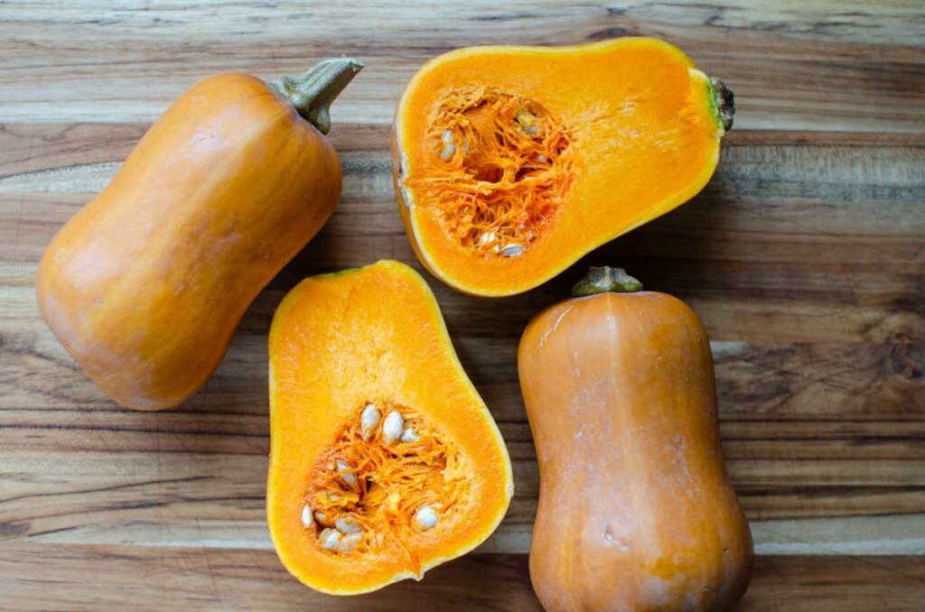 3 whole honeynut squash with one cut in half on a wood cutting board