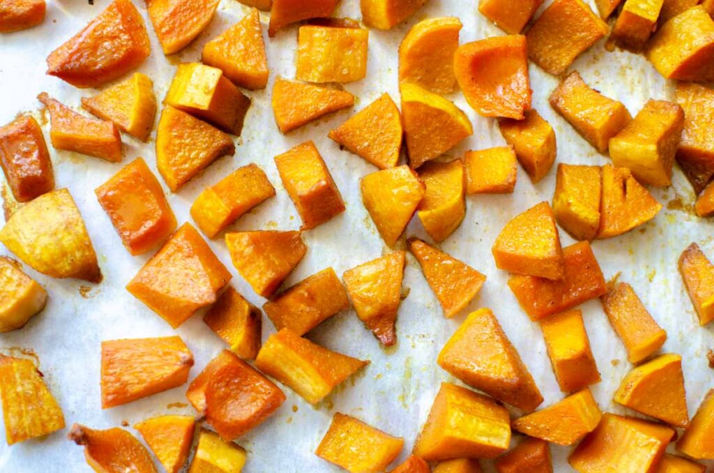 roasted curry flavored honeynut squash pieces on parchment lined baking sheet.