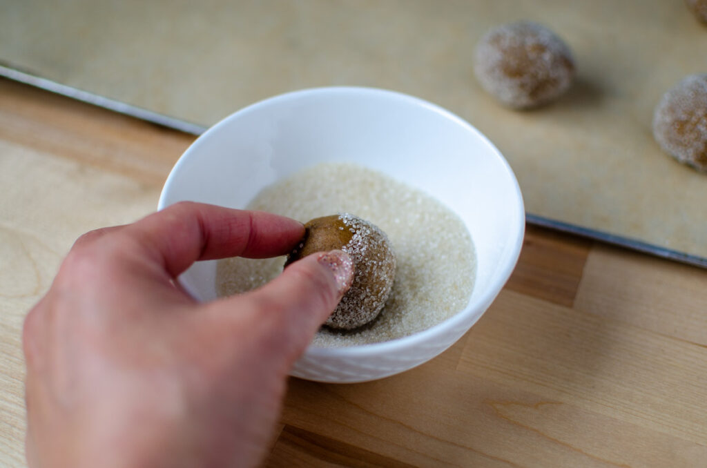 rolling sourdough molasses cookie dough ball in a small bowl of sugar