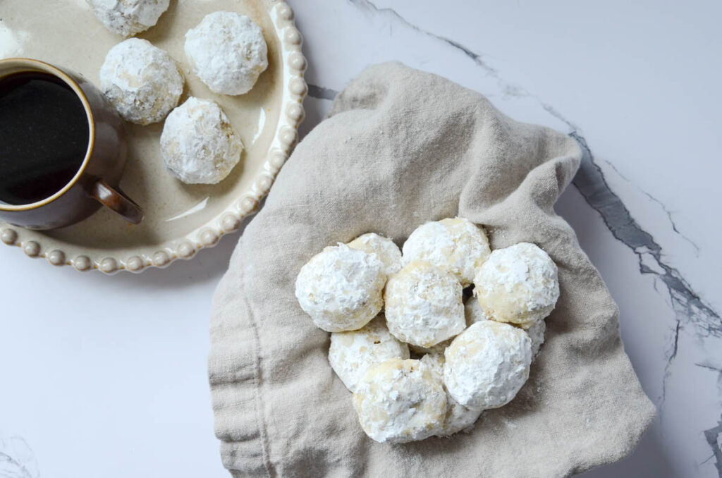 Sourdough Russian tea cake cookies on a towel-lined basket with a cup of coffee