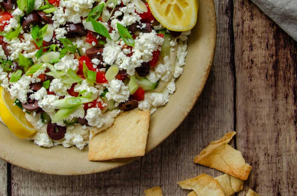 Greek hummus dip in shallow stone dish with pita chips