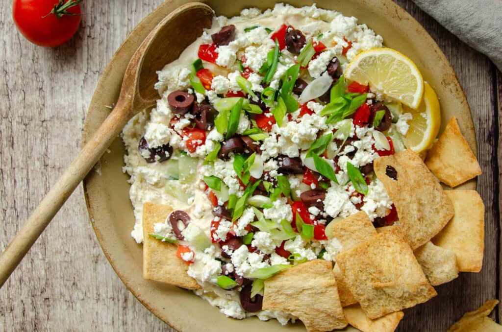 Mediterranean layer hummus dip in shallow pan with pita chips