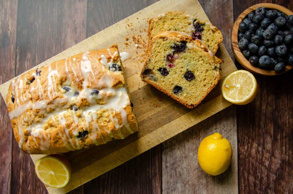 lemon blueberry sourdough bread slices on a wood cutting board with cut lemons and a bowl of blueberries