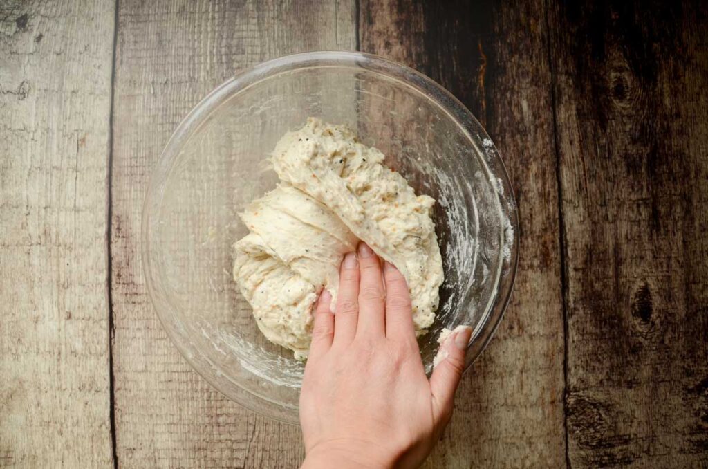 folding sourdough everything bread in a glass bowl