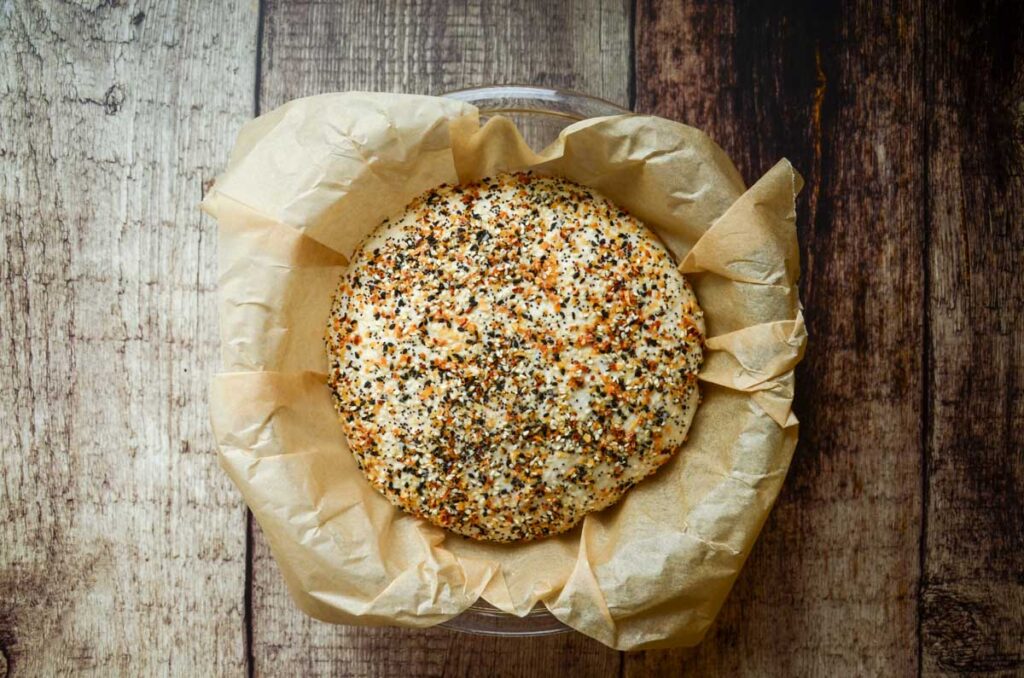 everything sourdough bread that's covered in everything bagel seasoning proofing in a parchment lined bowl