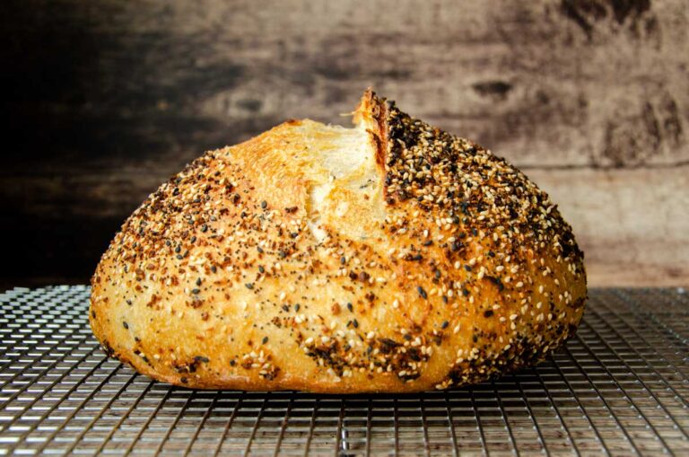 a loaf of sourdough everything bread on a wire rack