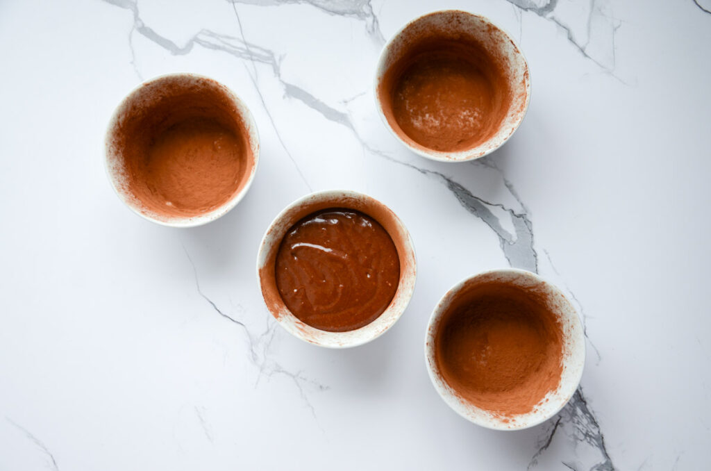 4 white ramekins dusted with cocoa powder and one filled with chocolate lava cake batter