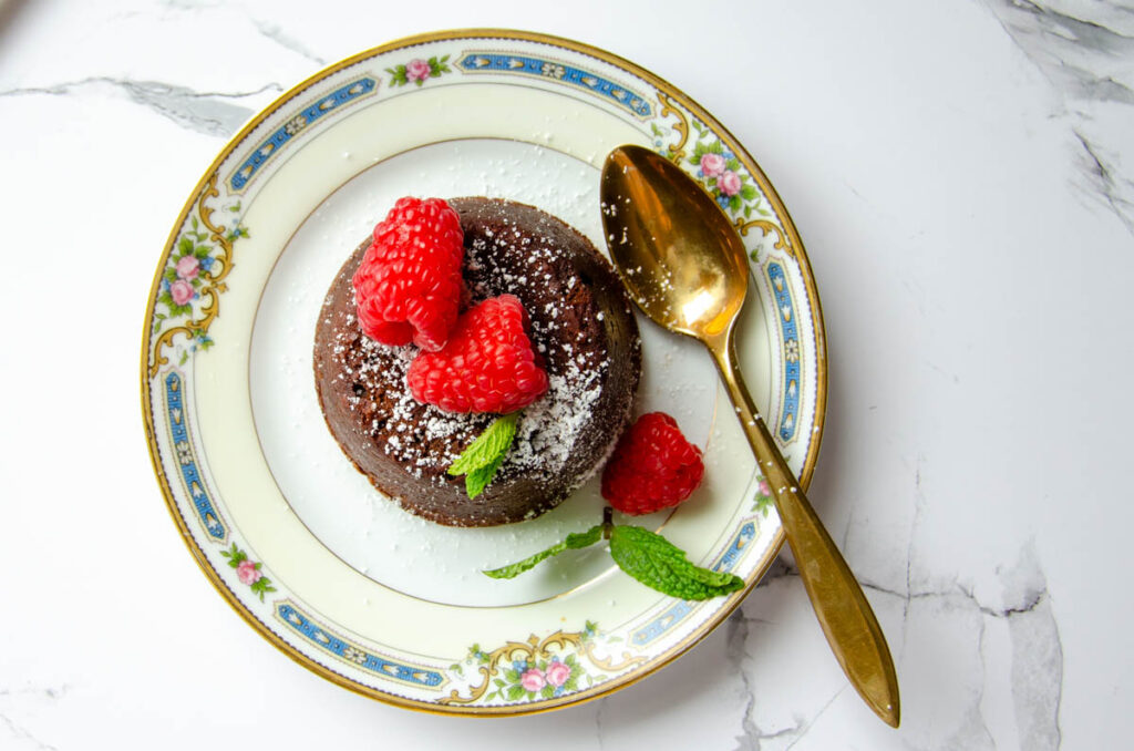 chocolate lava cake on a plate with a gold spoon and raspberries