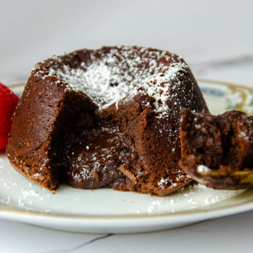 molten lava cake on a plate with a spoon and raspberry