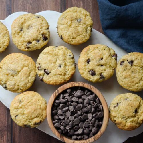 sourdough chocolate chip muffins on a marble tray with a wooden bowl of chocolate chips