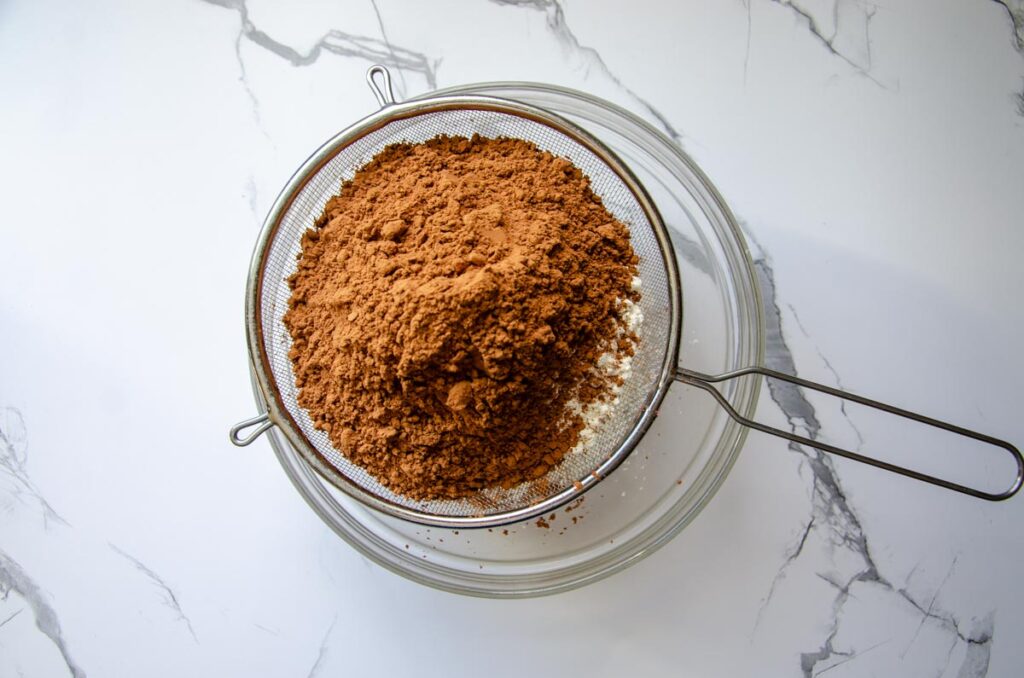 sifting dry ingredients for chocolate espresso cake through a wire mesh strainer