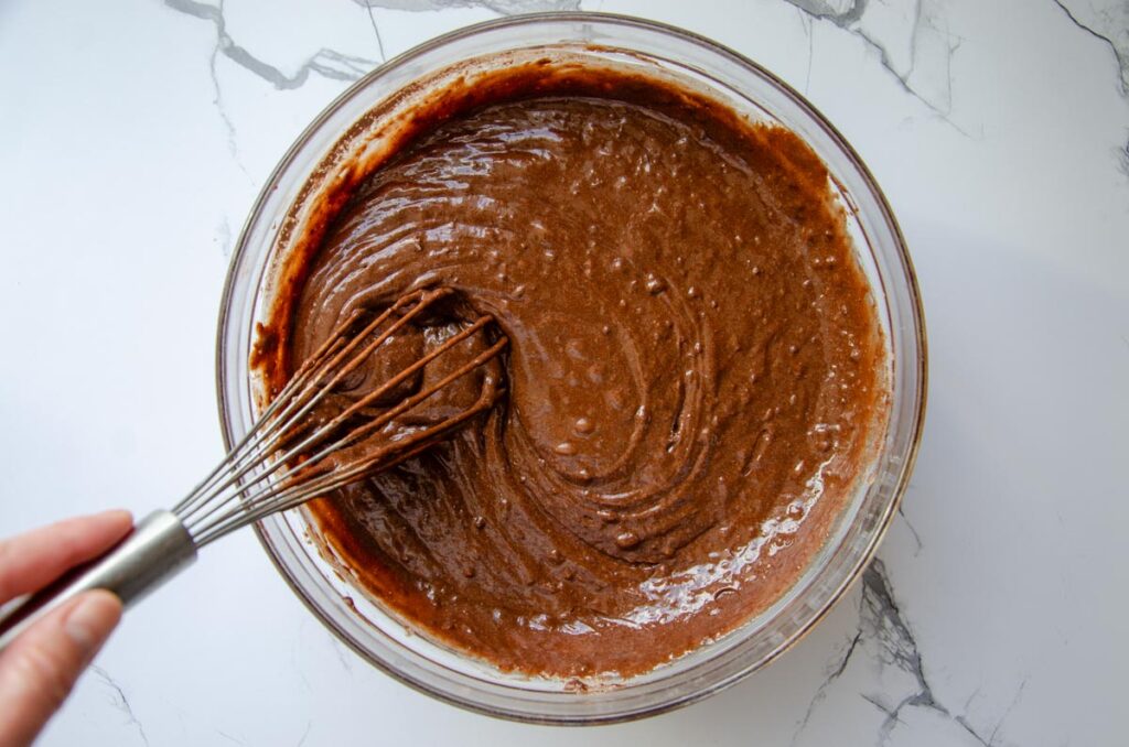 whisking chocolate cake batter in a glass bowl