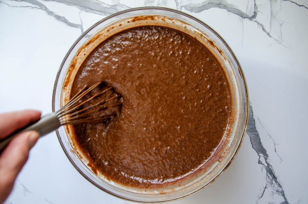 whisking the chocolate cake batter in a glass bowl