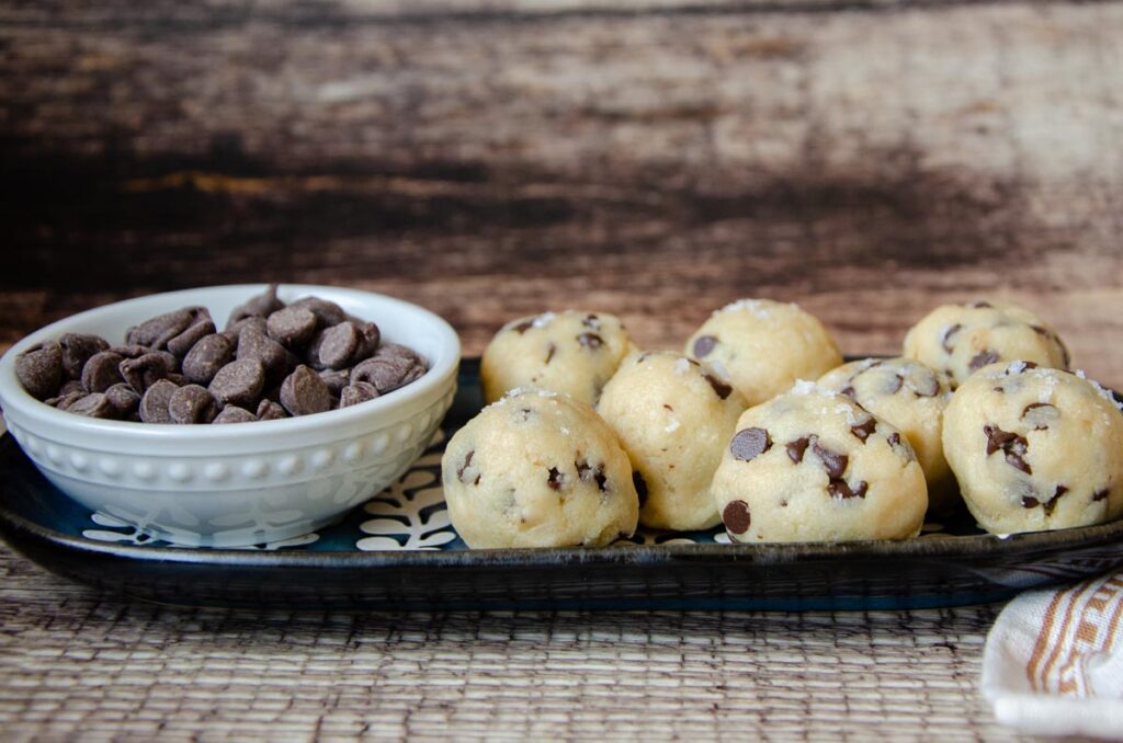 cookie dough balls on a serving plate with a bowl of chocolate chips