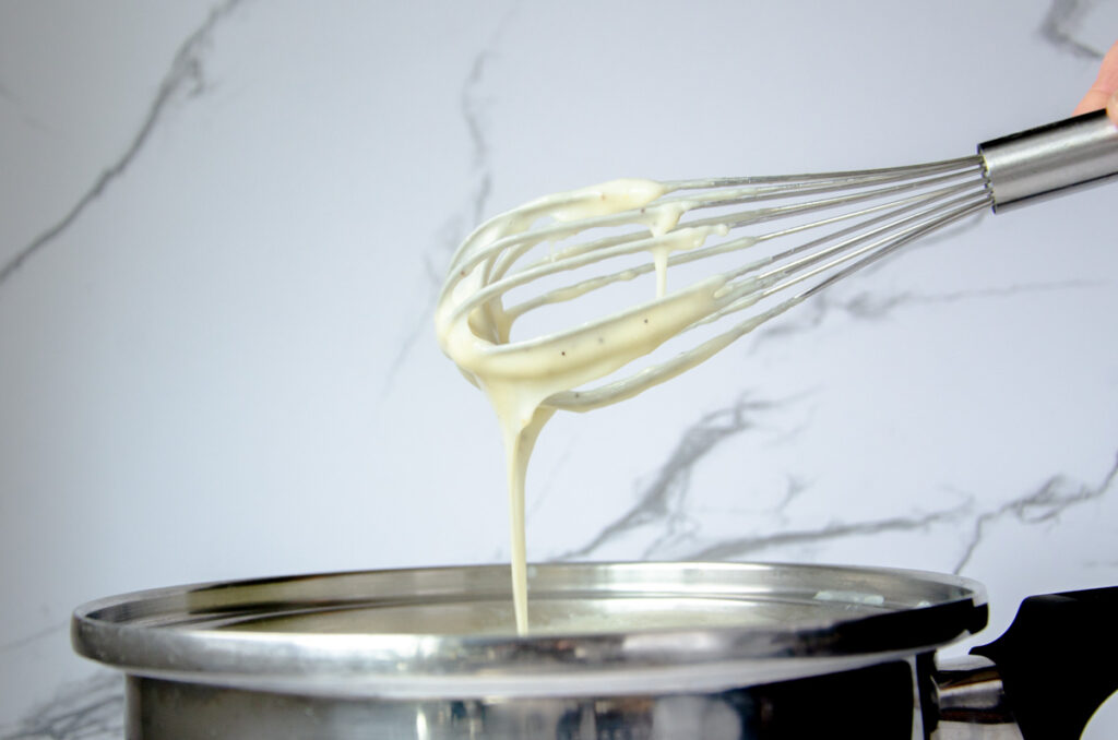 a whisk above a sauce pan with bechamel sauce