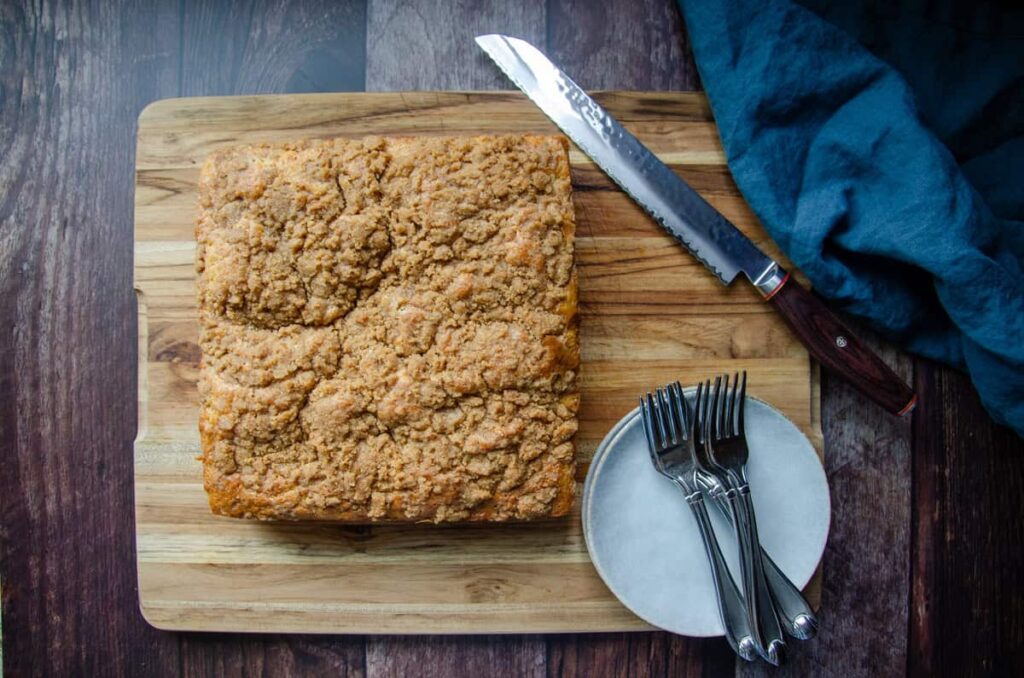 Sourdough coffee cake on a wooden board with plates, forks, and a large knife