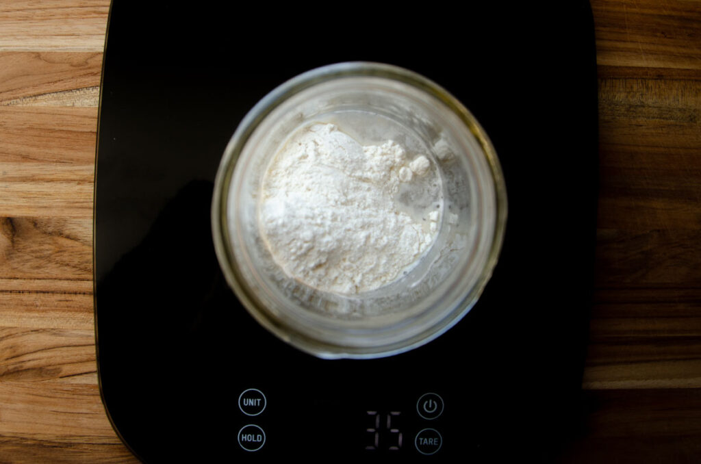 water and flour in a jar of dried sourdough on a black scale