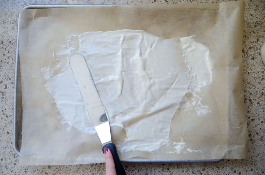 spreading sourdough starter onto a piece of parchment paper with an offset spatula 