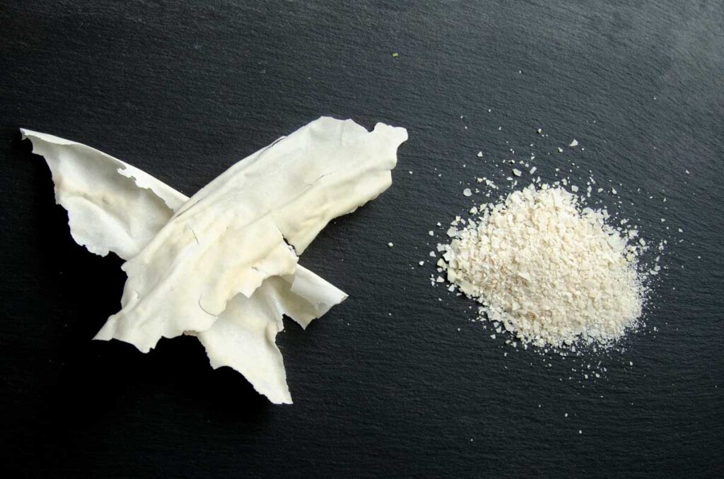 flakes of dried sourdough starter and powdered starter on a black slate plate