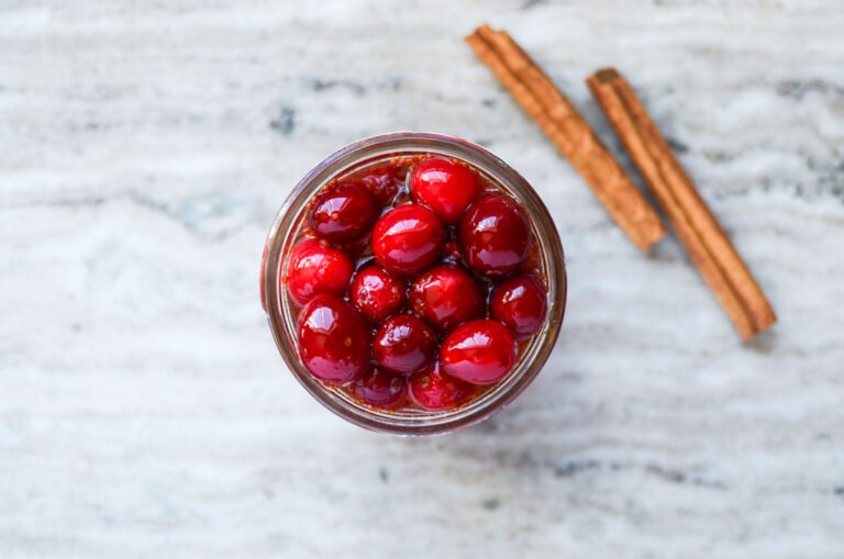 honey fermented cranberries in a jar next to a few cinnamon sticks