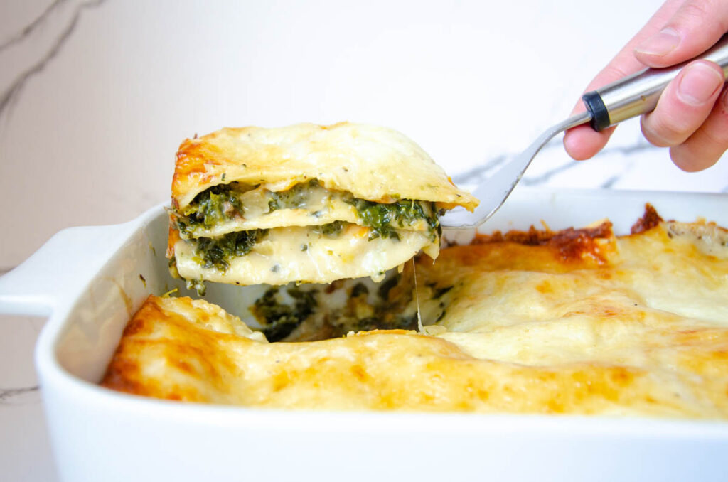 lifting a piece of vegetable lasagna with white sauce with a spatula