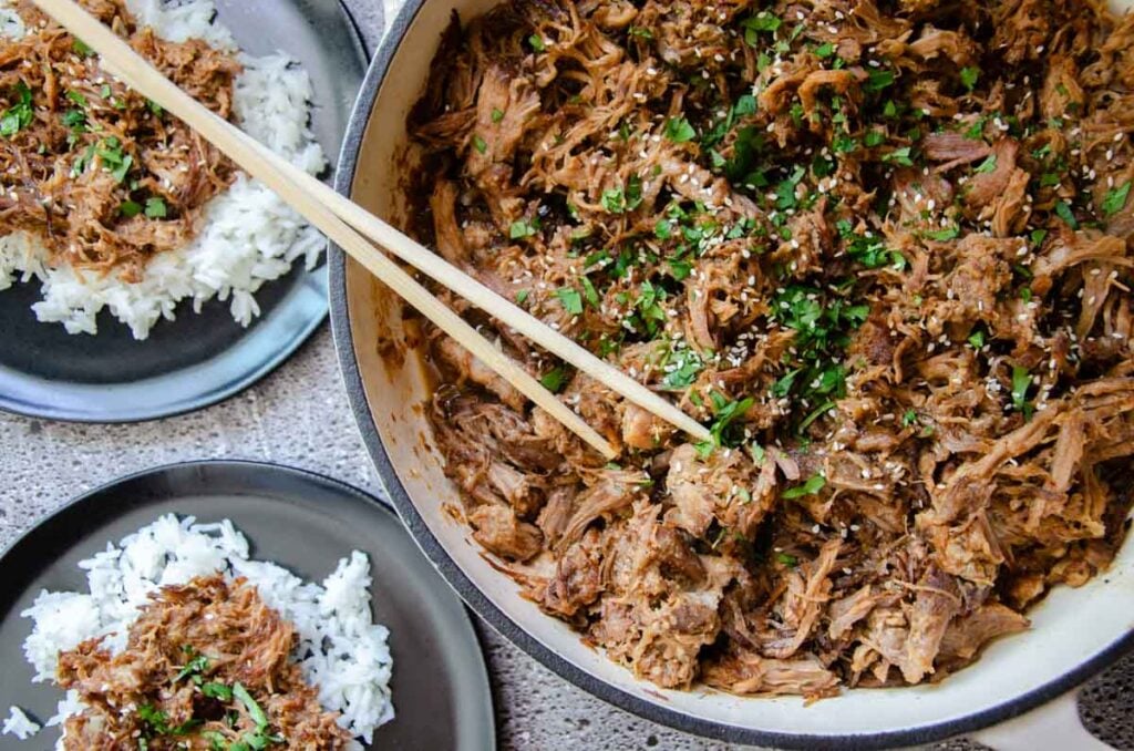 Korean pulled pork in a large skillet, and small plates next to it.