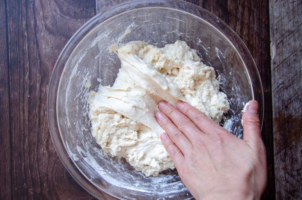 folding the sourdough bread dough over onto itself in a glass bowl