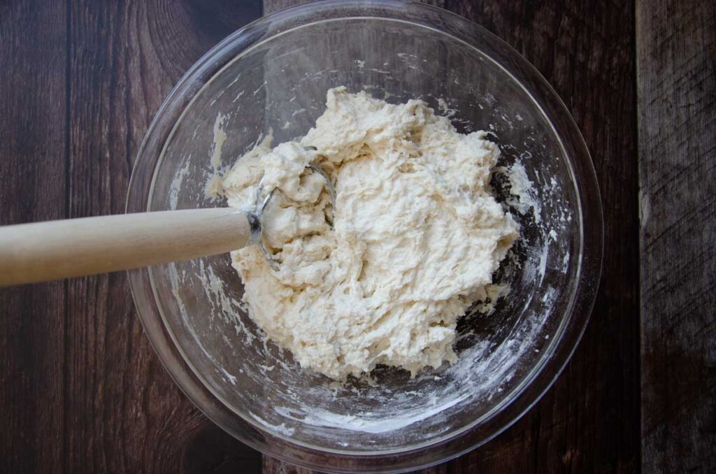 sourdough bread dough in a glass bowl with a Danish dough whisk