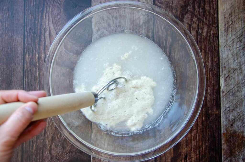 stirring sourdough starter and water in glass bowl