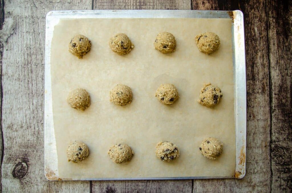 scooped sourdough chocolate chip oatmeal cookie dough on parchment lined baking sheet. 