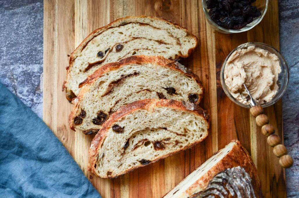 slices of sourdough cinnamon raisin bread on a cutting board with a small dish of butter and raisins