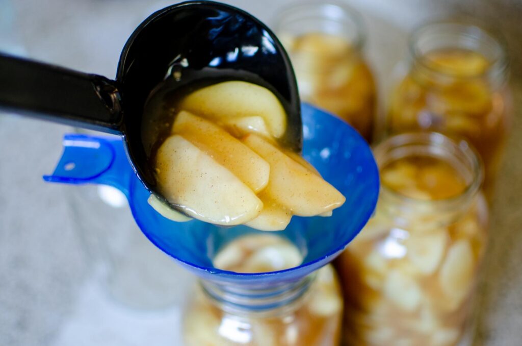 ladling apple pie filling into a glass jar