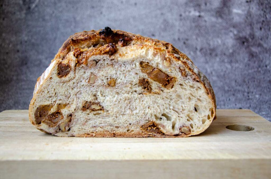 A cut loaf of fig and walnut sourdough bread on a wood cutting board