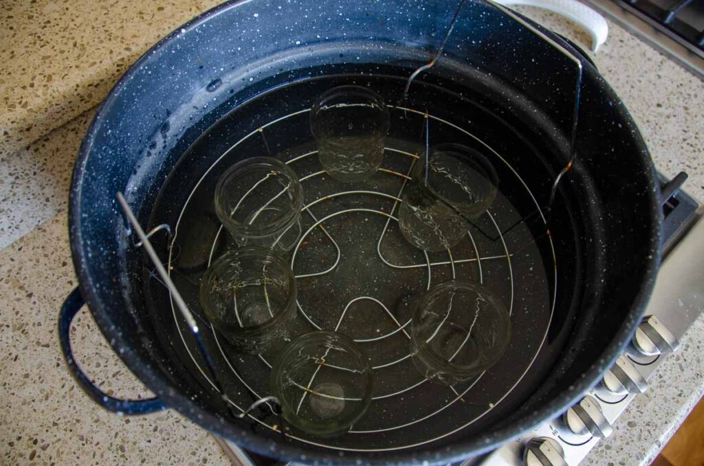 A water bath canner filled with water and empty jars