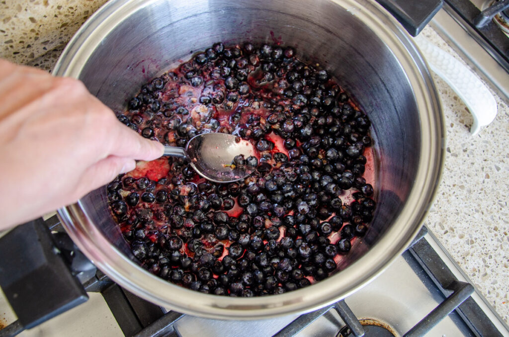 mashing blueberries with a spoon in a large pot on the stove