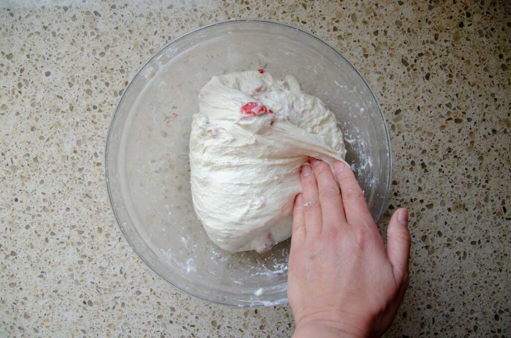 folding sourdough strawberry bread dough in a glass bowl