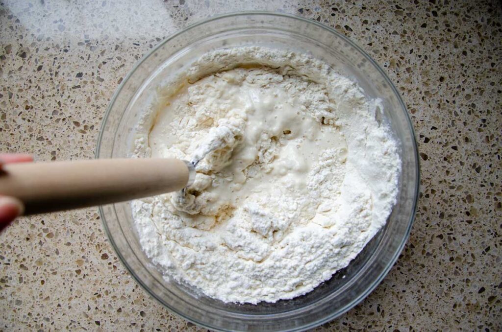 sourdough bread ingredients in a glass mixing bowl with a Danish dough whisk