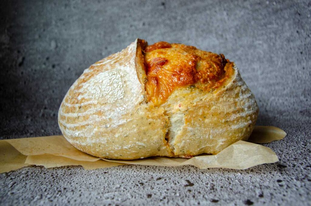 a loaf of pepperoni sourdough bread on a piece of parchment paper