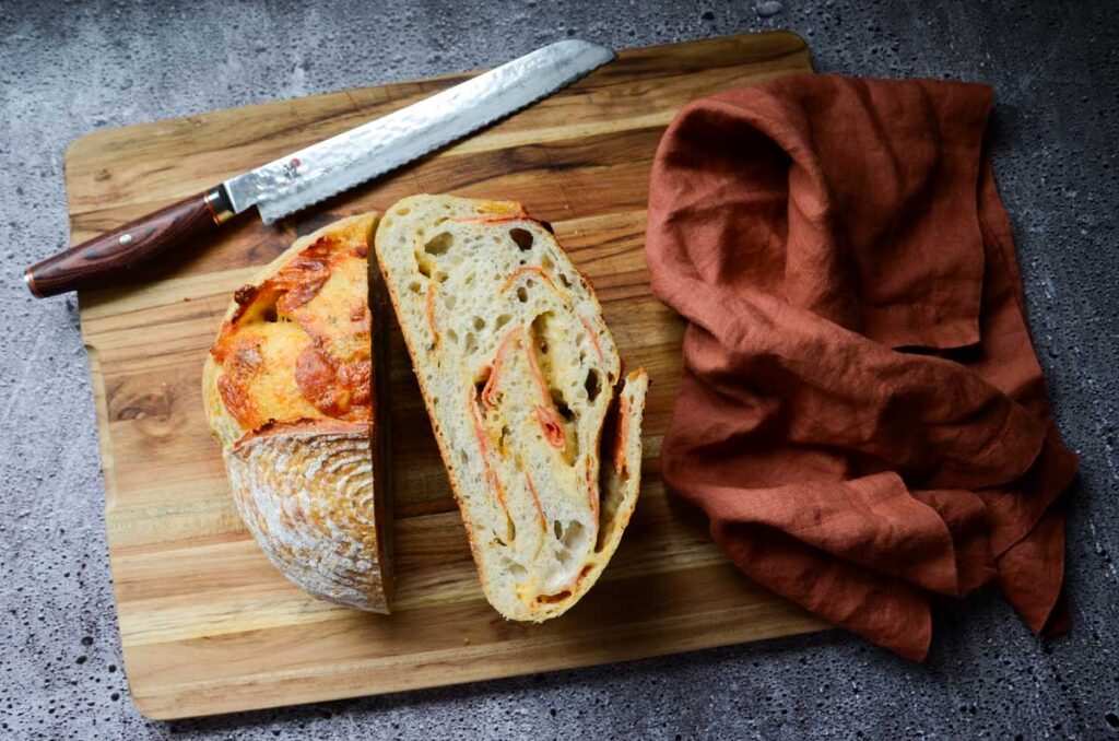 sourdough pepperoni bread cut in half on a wood cutting board with a knife and napkin