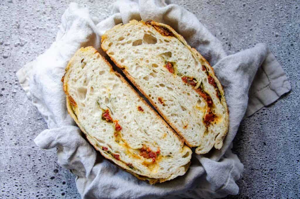 a cut loaf of sourdough pesto sun dried tomato bread in a lined basket