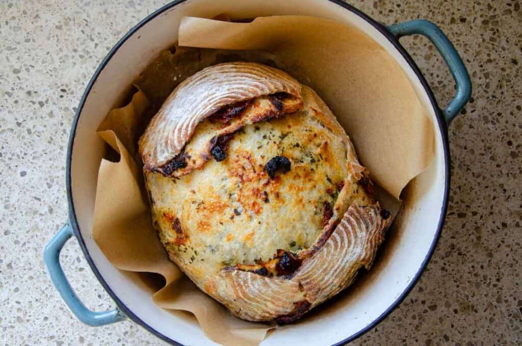 a loaf of sourdough sundried tomato pesto bread in a Dutch oven.