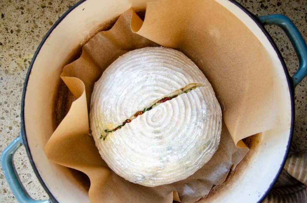 lifting the parchment lined bread dough into a hot Dutch oven