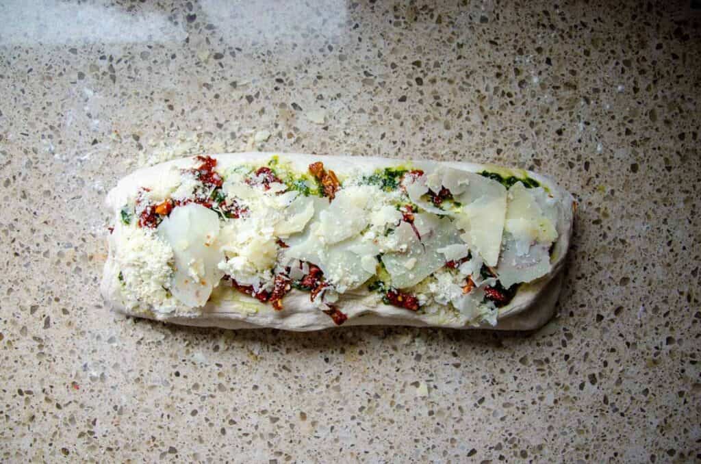 adding more cheese, pesto and sun dried tomatoes to the top layer of the dough