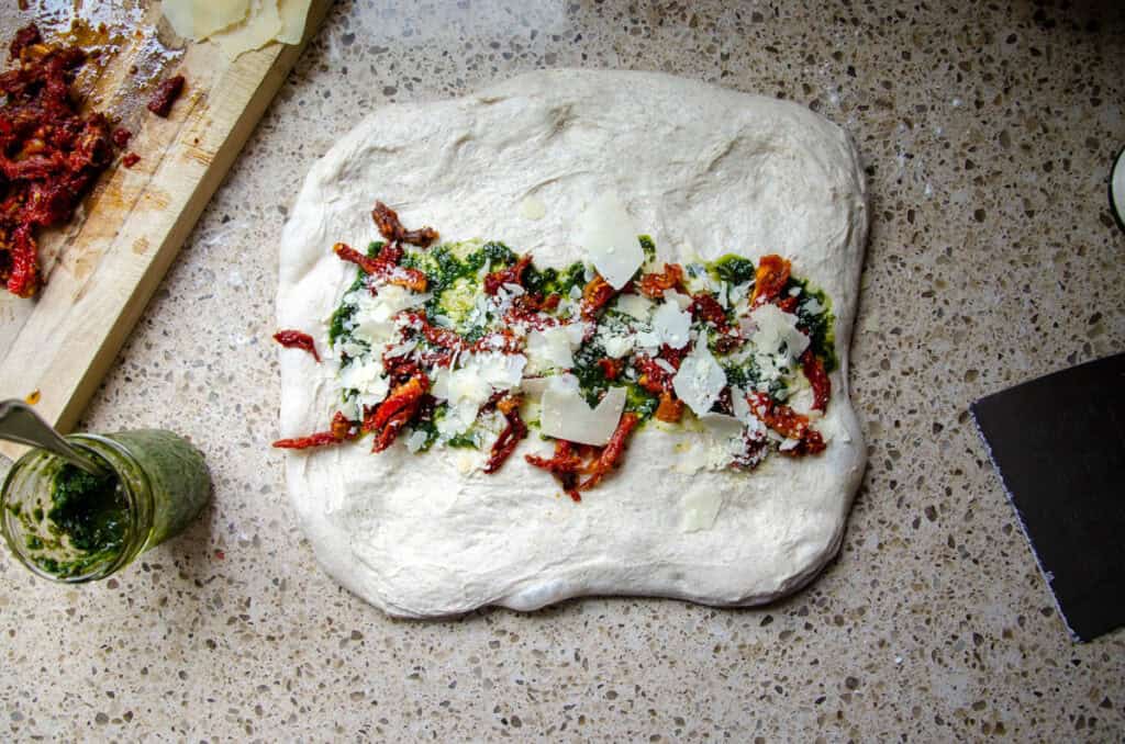 spreading tomatoes, pesto, and cheese down the center of the dough