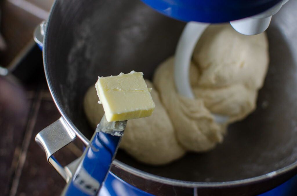 adding pats of butter to the bowl of a stand mixer with sourdough sandwich bread dough