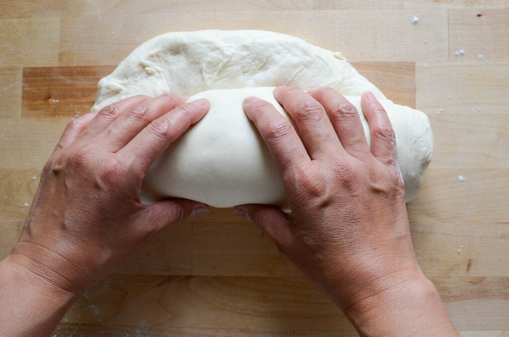 rolling out the sourdough sandwich bread dough into a log with both hands