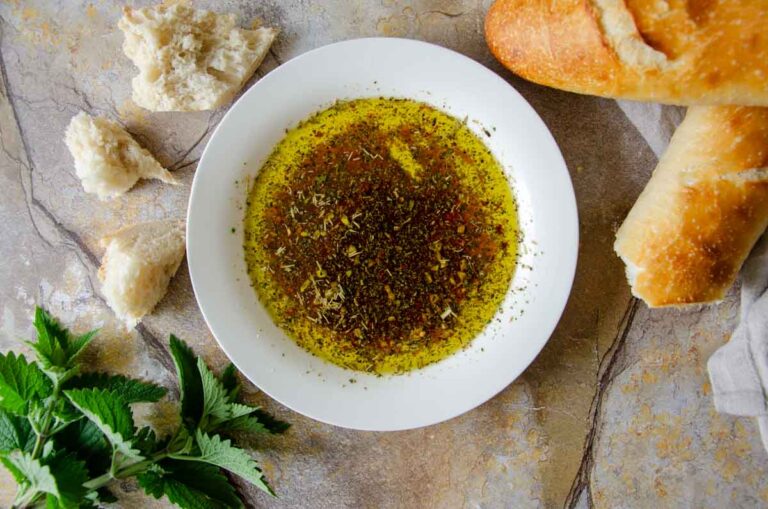 Bowl of dipping oil surrounded by fresh bread and herbs
